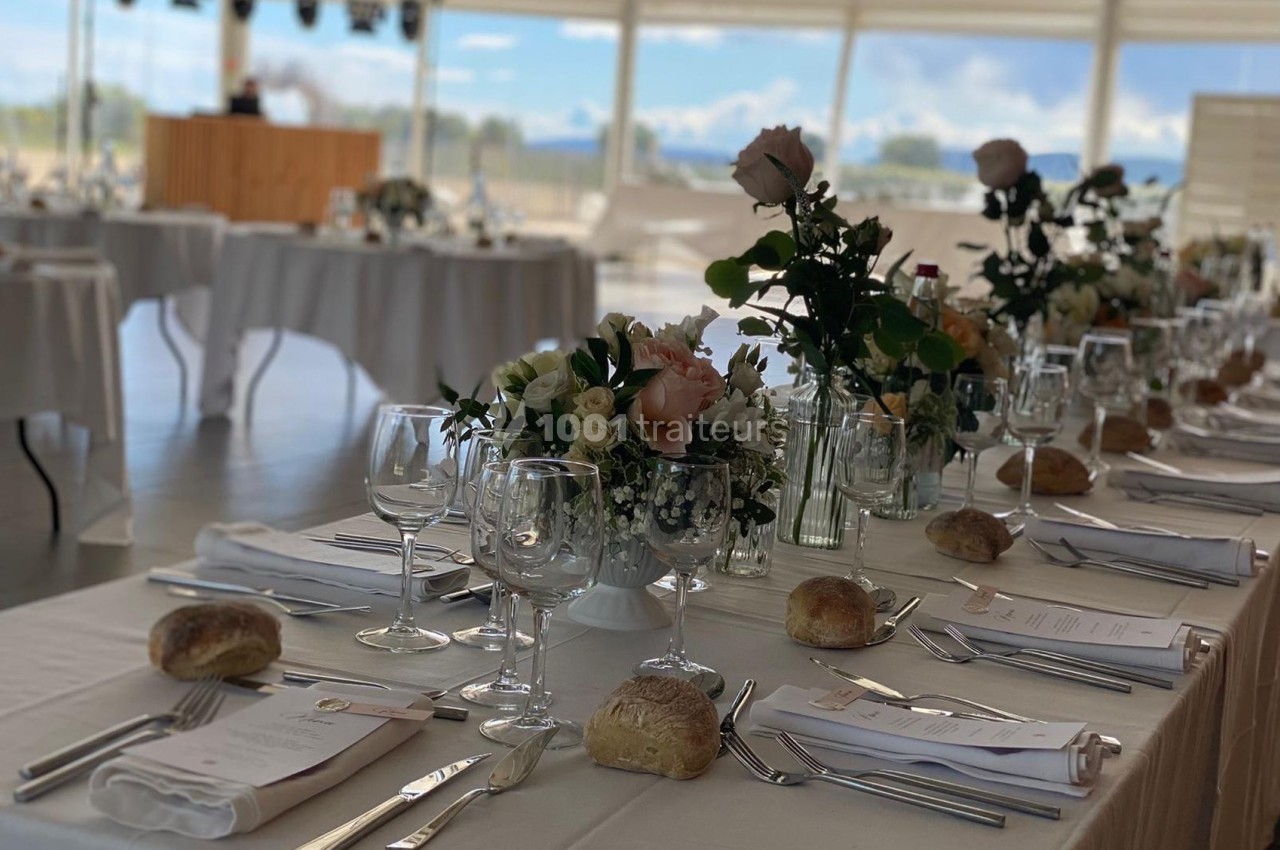 Table dressée pour un repas festif avec nappes blanches, fleurs, verres, couverts et petits pains.