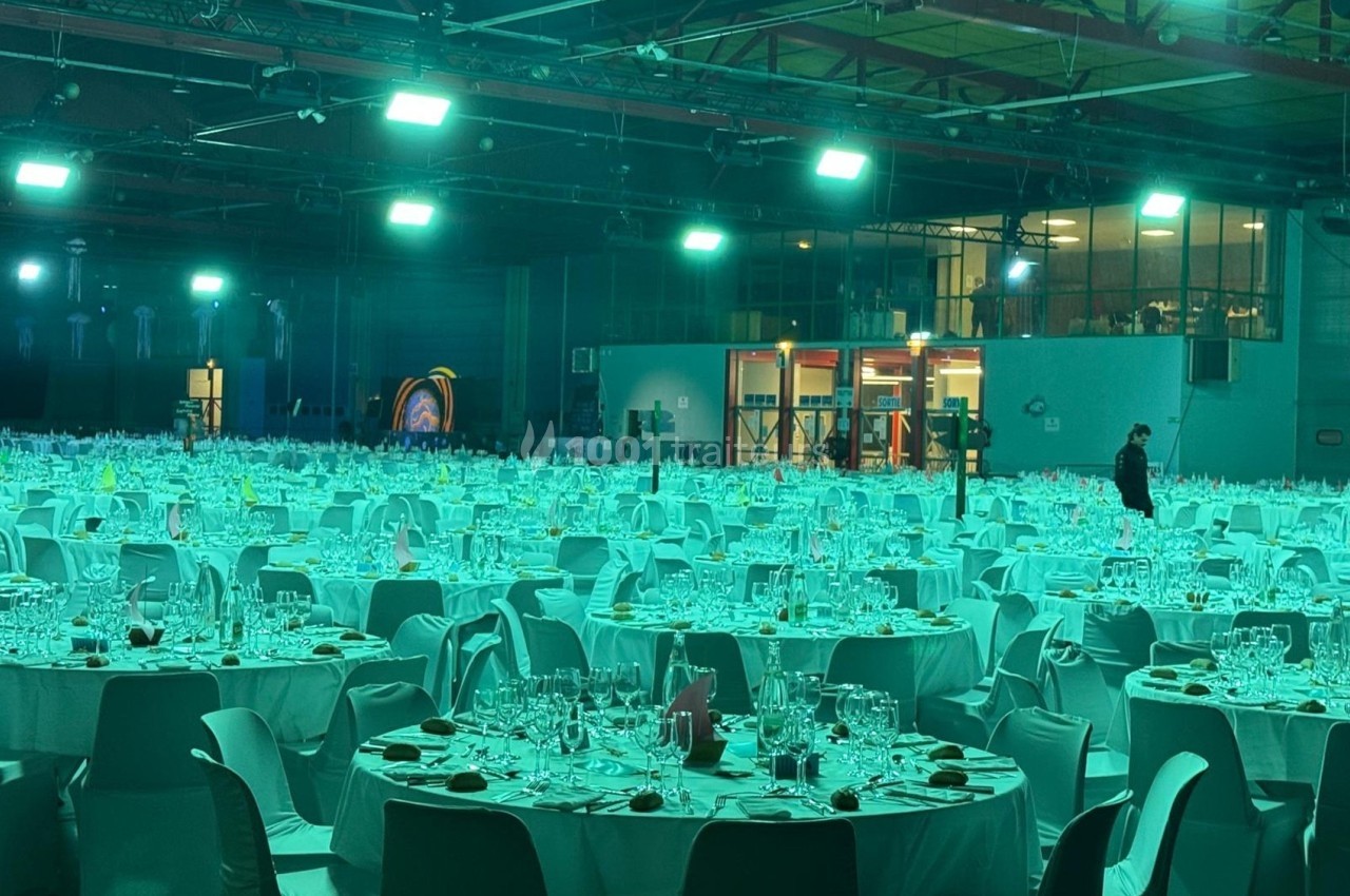 Salle de réception avec de nombreuses tables rondes dressées pour un événement, éclairée par des lumières vertes.