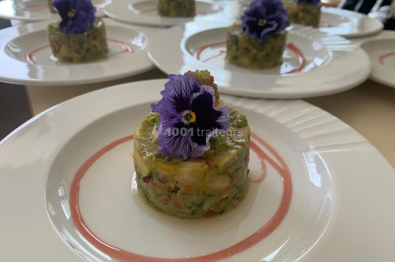 Tartare de légumes dressé en cercle, décoré d'une fleur comestible violette, servi sur une assiette blanche.