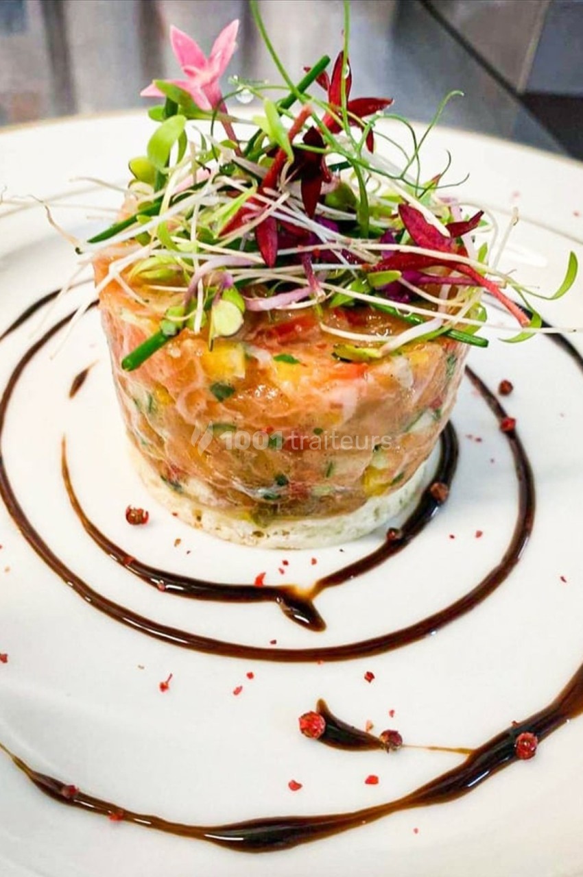 Tartare de saumon dressé avec des pousses et des herbes fraîches, entouré de traits de sauce balsamique.