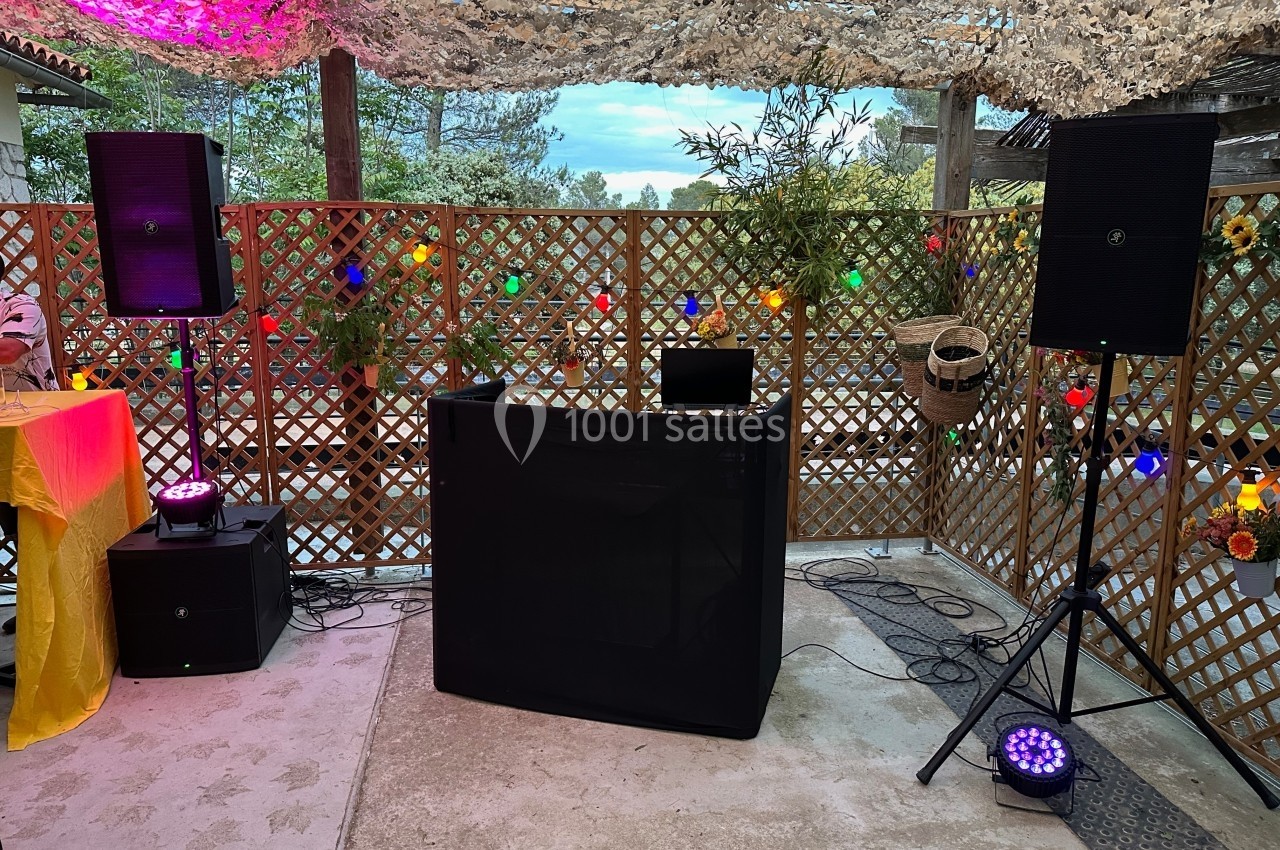 Installation de matériel DJ avec enceintes, table de mixage et éclairages colorés sous une pergola décorée.