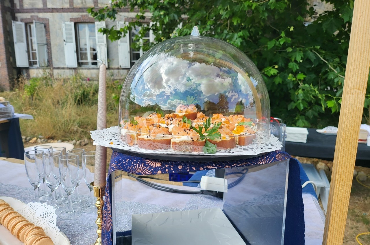 Plateau de canapés apéritifs sous une cloche en verre, disposé sur une table dressée en extérieur.