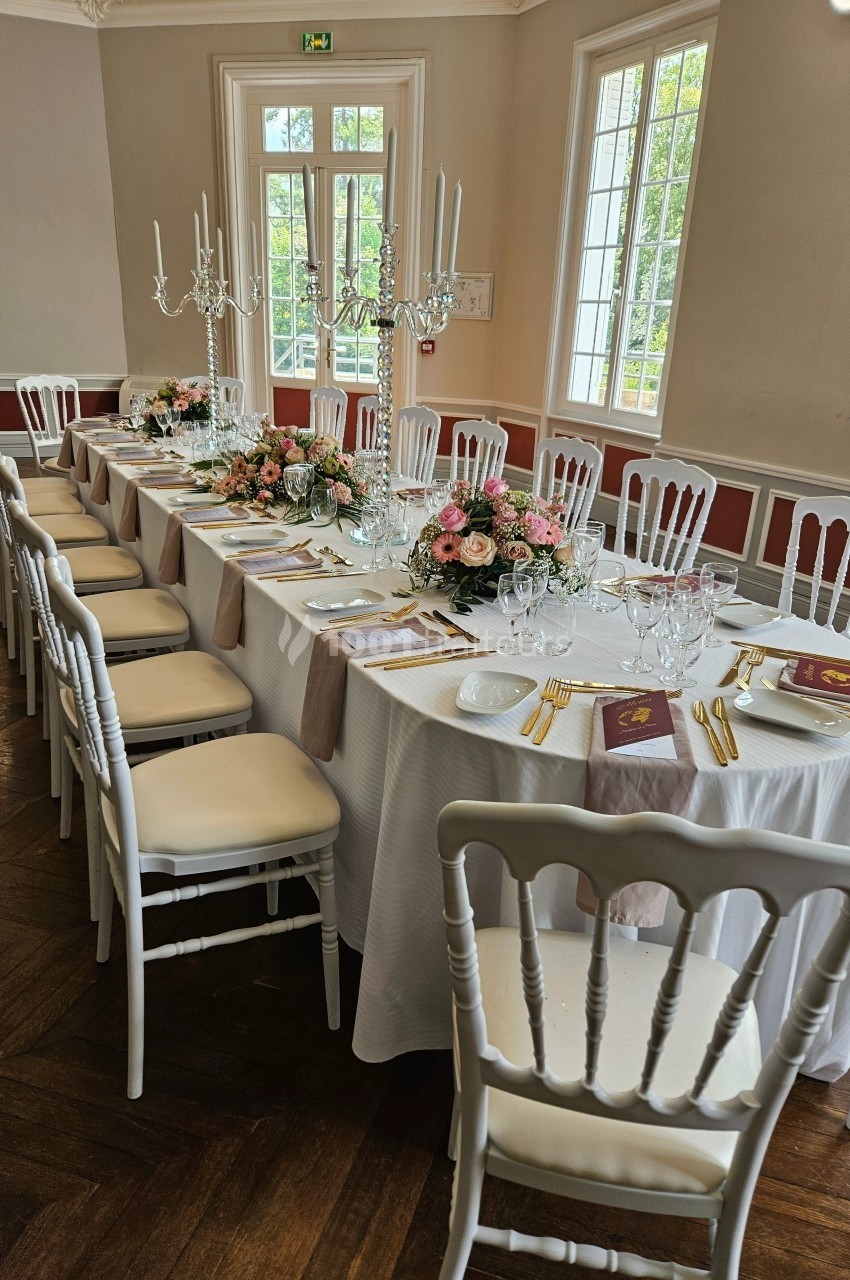Table élégamment dressée pour un repas, avec nappes blanches, chandeliers, fleurs et vaisselle raffinée dans une salle…
