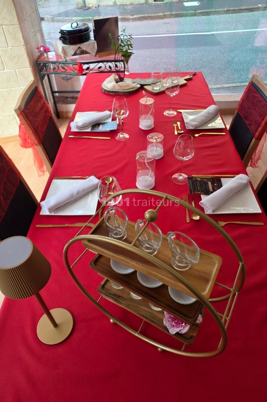 Table dressée avec une nappe rouge, vaisselle élégante, verres, serviettes pliées et un présentoir décoratif au centre.