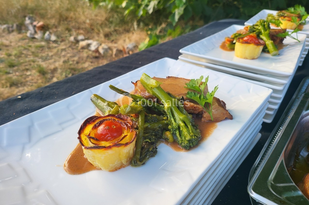 Assiette gastronomique avec viande, brocolis, roulé de pomme de terre et tomate cerise, servie en extérieur.