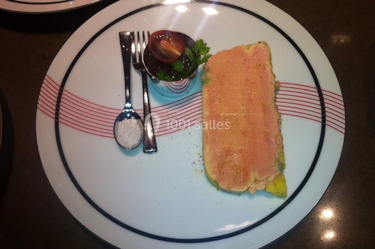 Tranche de terrine servie avec une tomate cerise, du persil, une cuillère de sel et des couverts sur une assiette décorée.