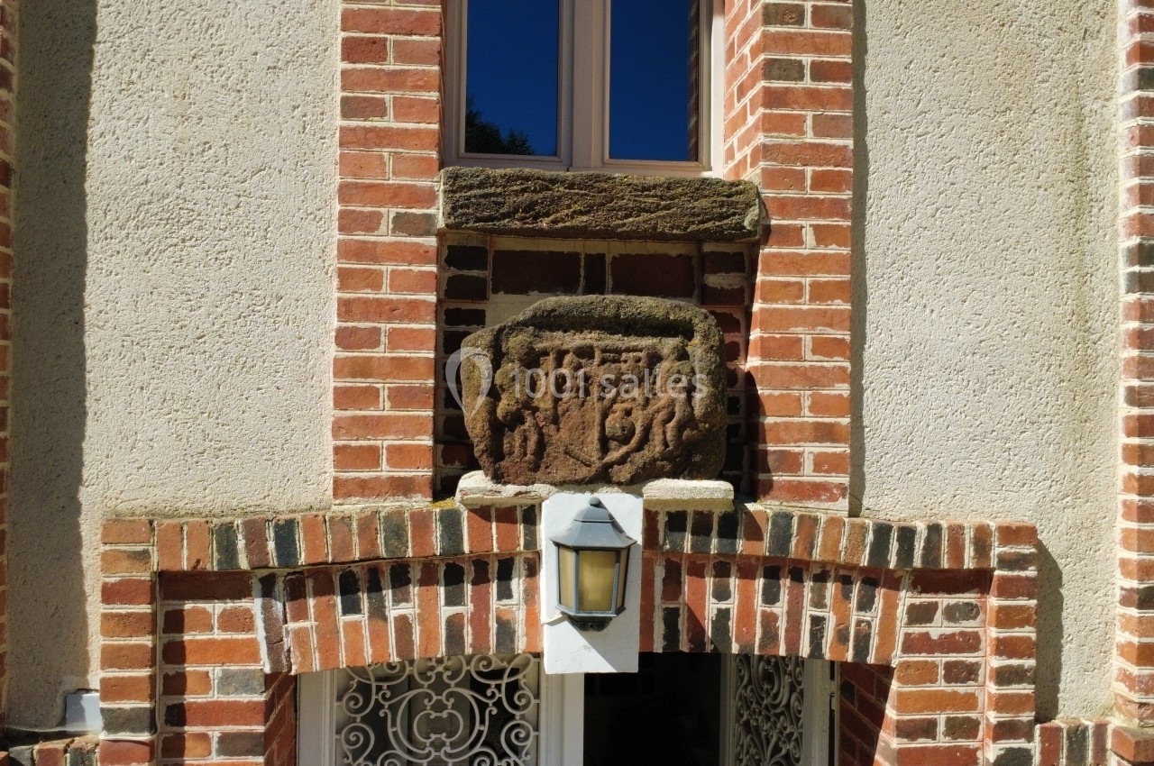 Détail architectural en briques avec une sculpture en pierre et une lanterne fixée au-dessus d'une fenêtre.
