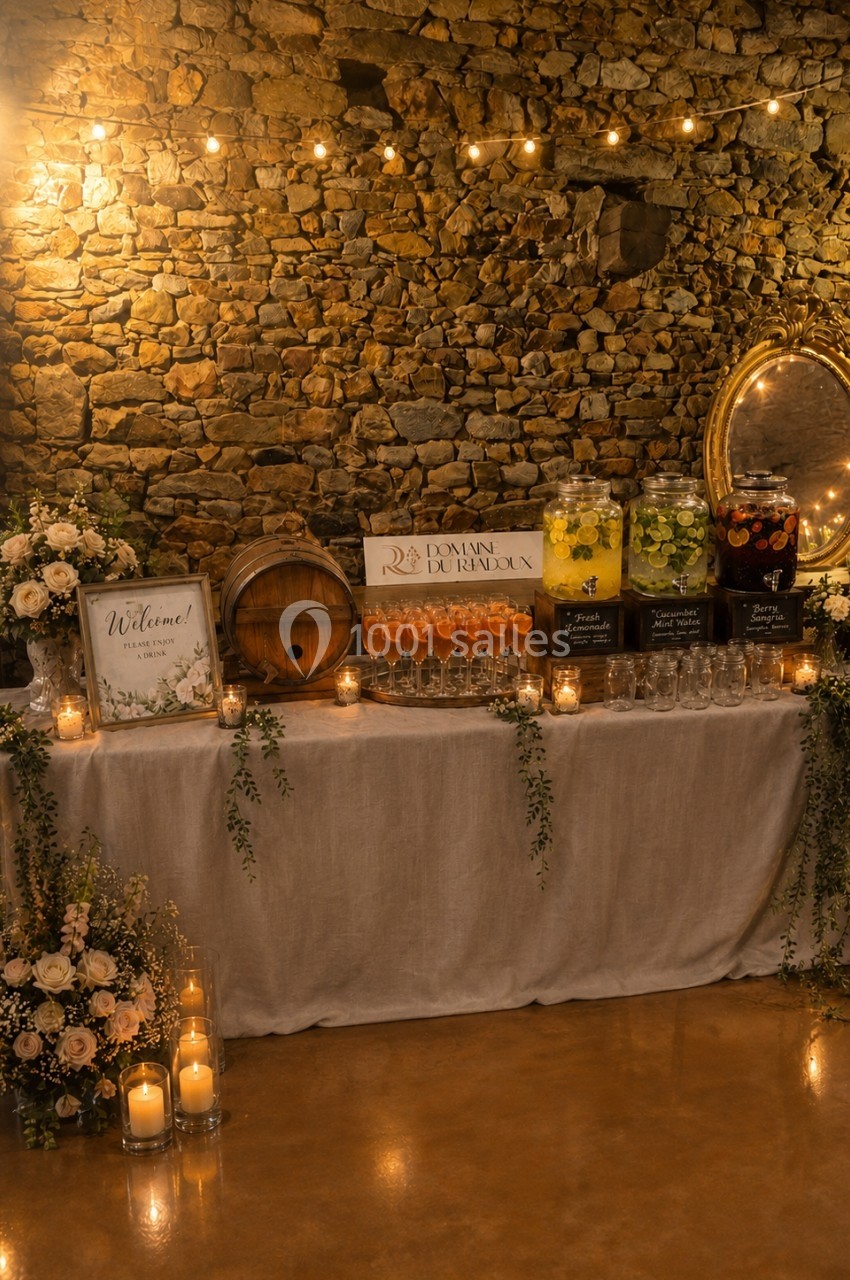 Table décorée pour un événement avec fleurs, bougies, boissons et un mur de pierre en arrière-plan.