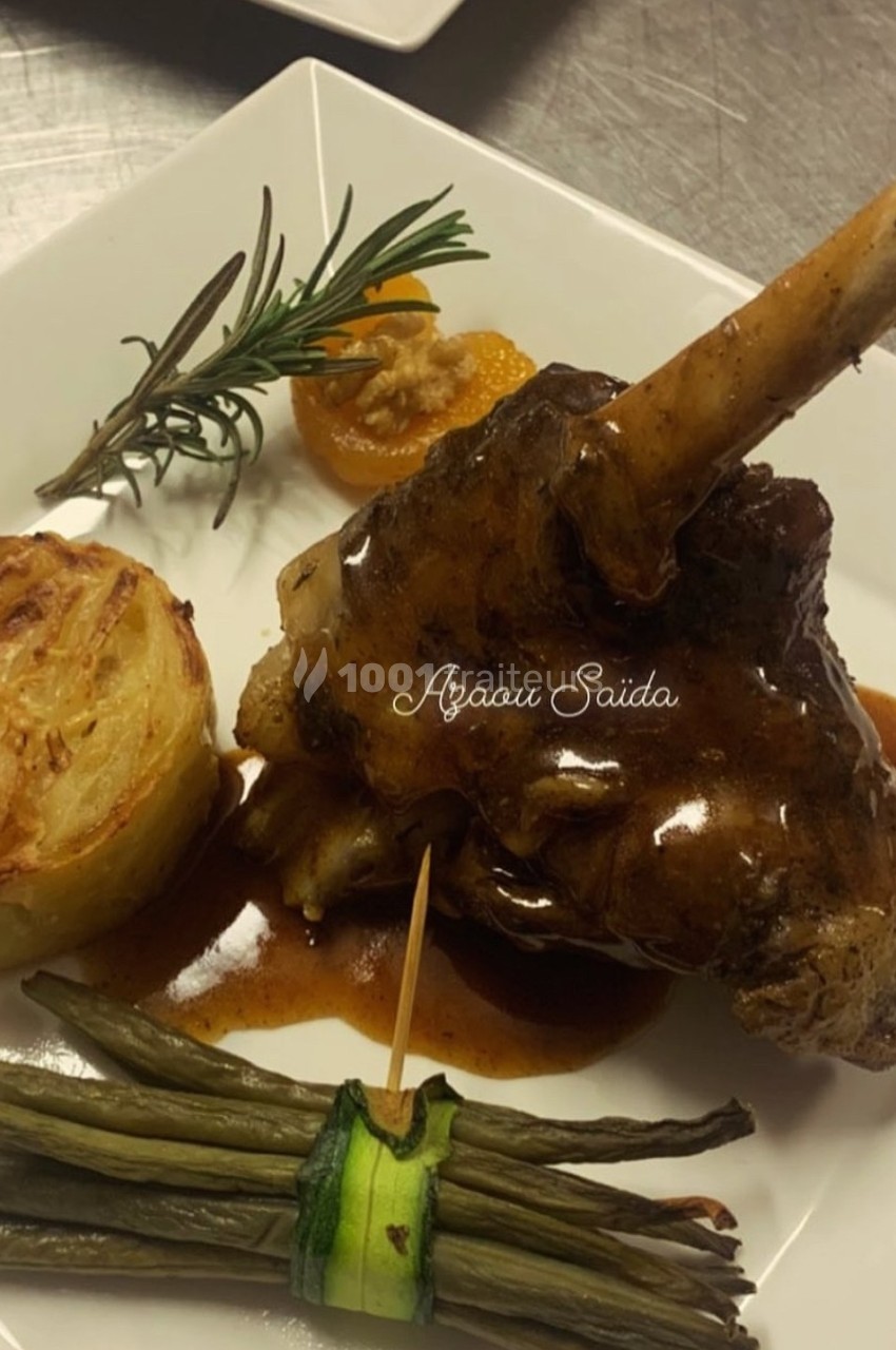 Plat composé d'un jarret d'agneau en sauce, accompagné de haricots verts, d'un gratin et d'une garniture décorative.