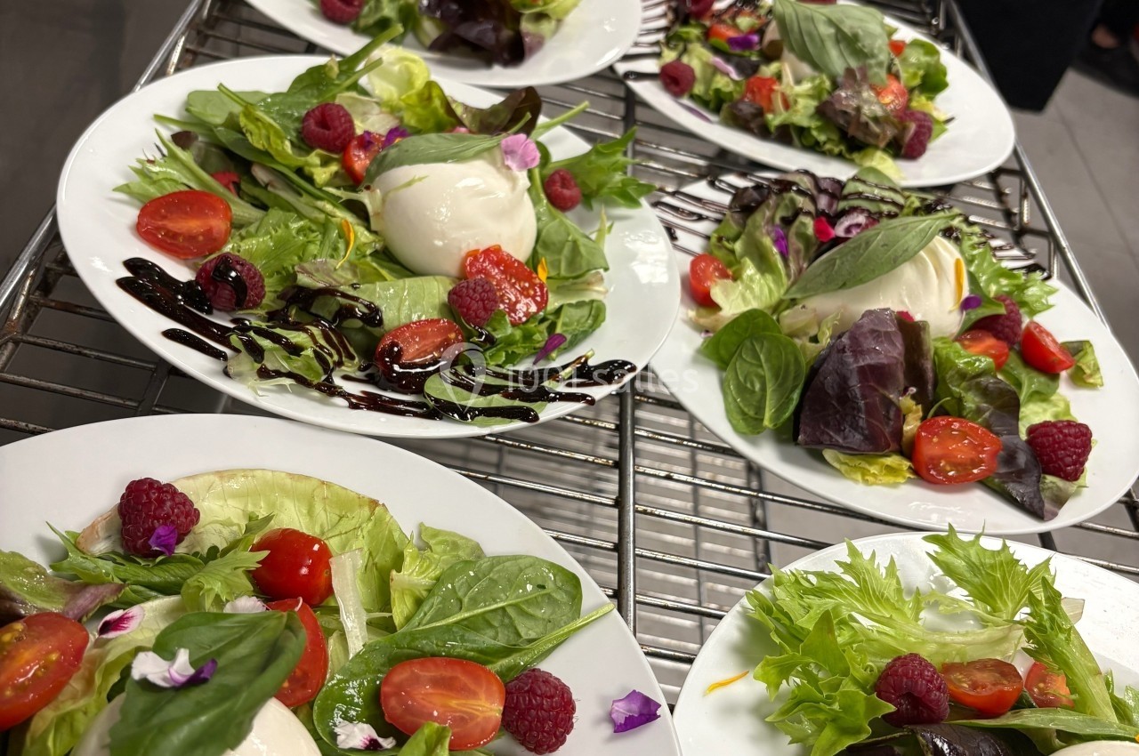 Assiettes de salade garnies de burrata, tomates cerises, framboises, feuilles de basilic et filet de vinaigre balsamique.