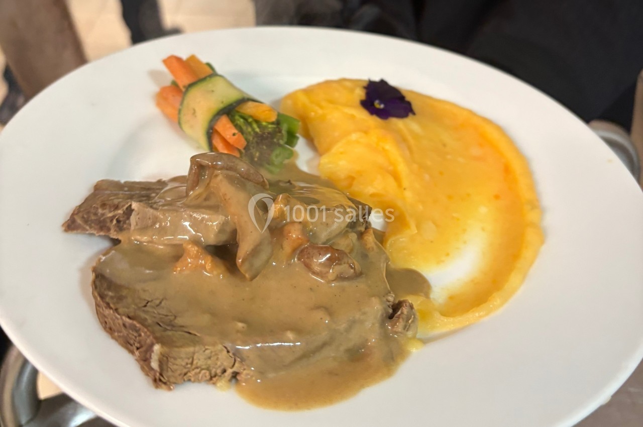 Assiette contenant une tranche de viande en sauce, une purée de pommes de terre et des légumes décorés d'une fleur…