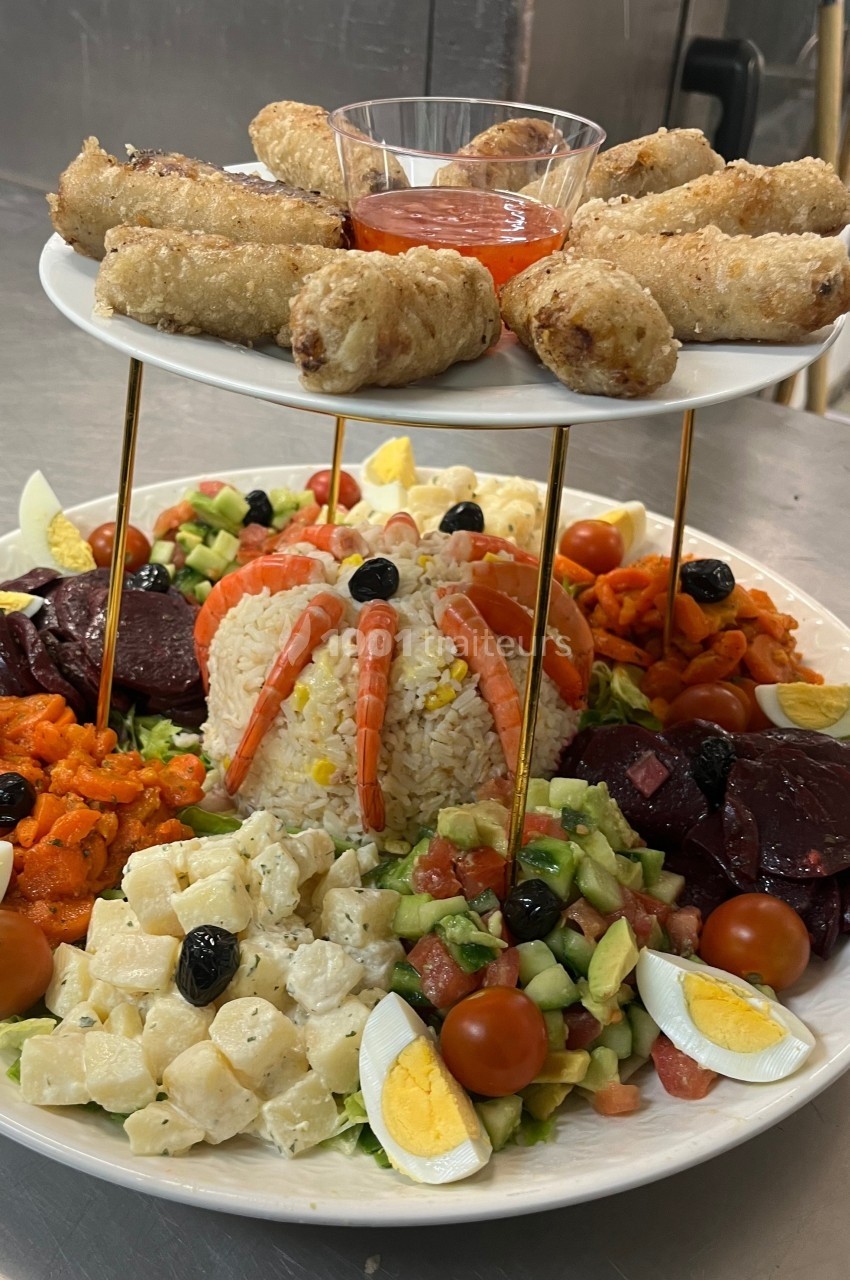 Assiette garnie de salades variées, riz décoré de crevettes, œufs, légumes et nems accompagnés de sauce.
