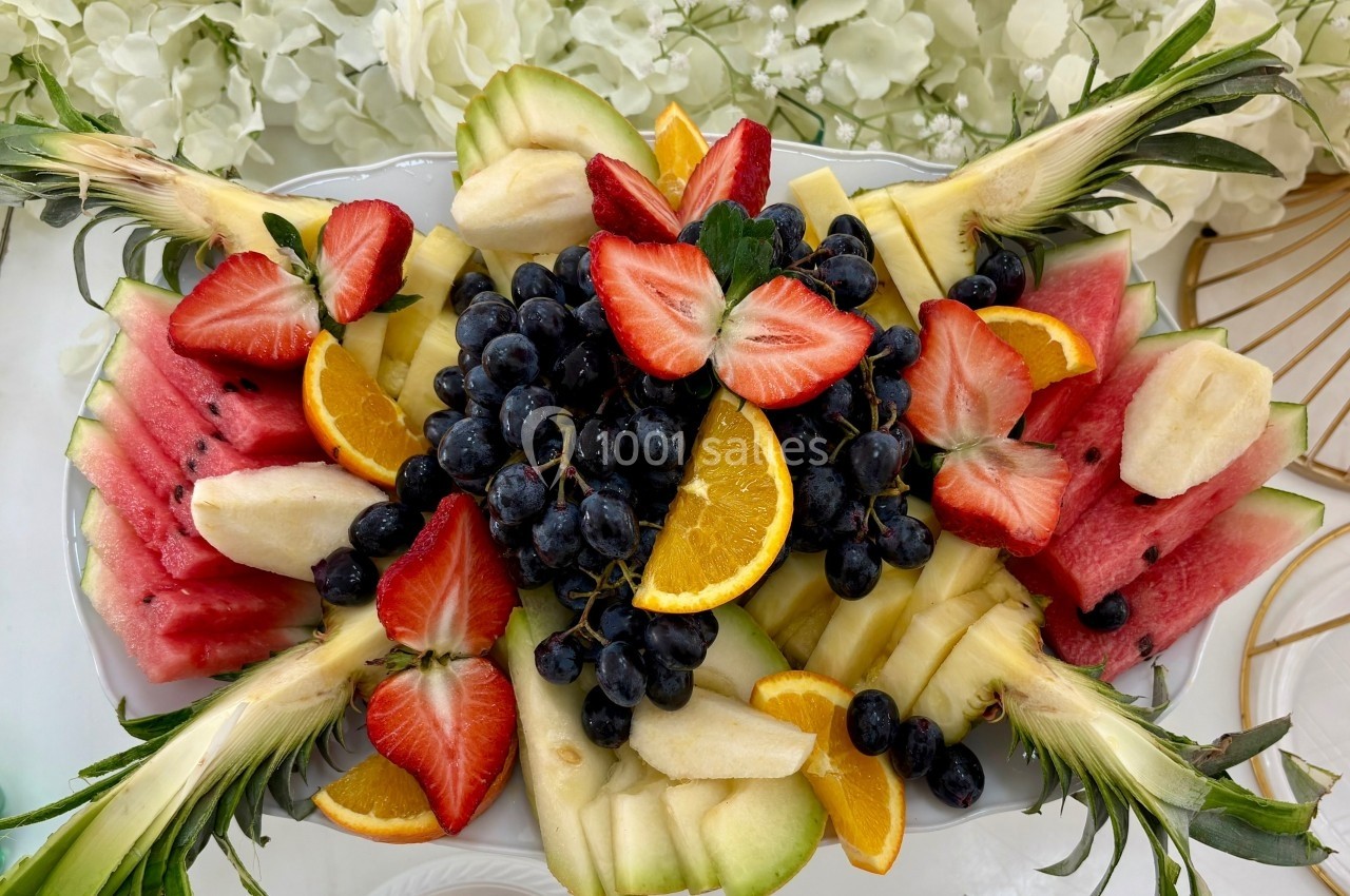Assortiment de fruits frais comprenant fraises, raisins, pastèque, ananas, bananes et tranches d'orange sur un plateau.