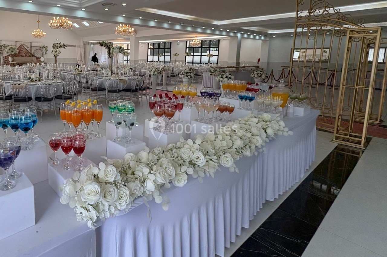 Table décorée avec des fleurs blanches et des verres colorés alignés, dans une grande salle de réception élégante.