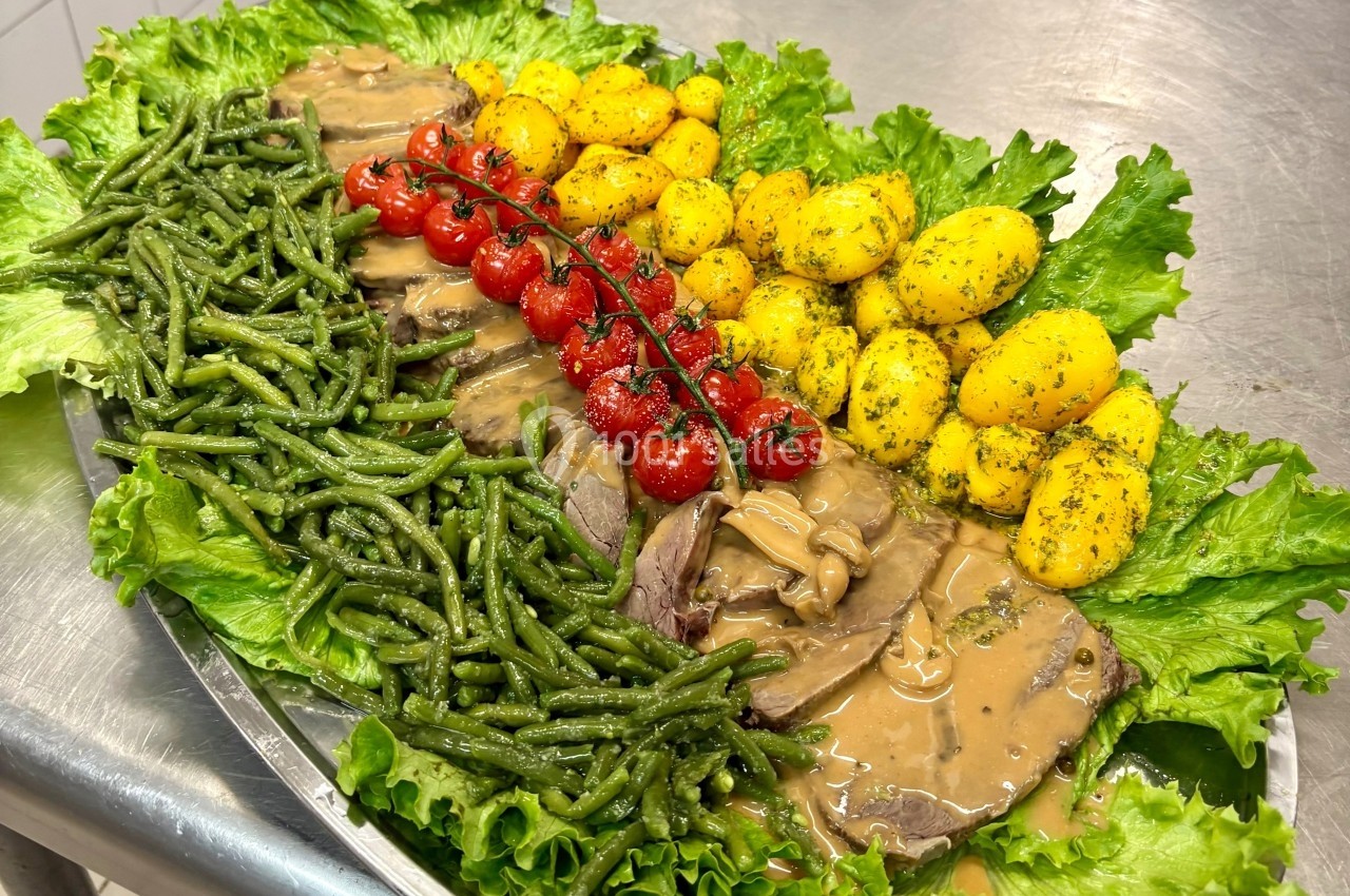 Plateau garni de rôti en sauce, haricots verts, pommes de terre persillées, tomates cerises et feuilles de salade.