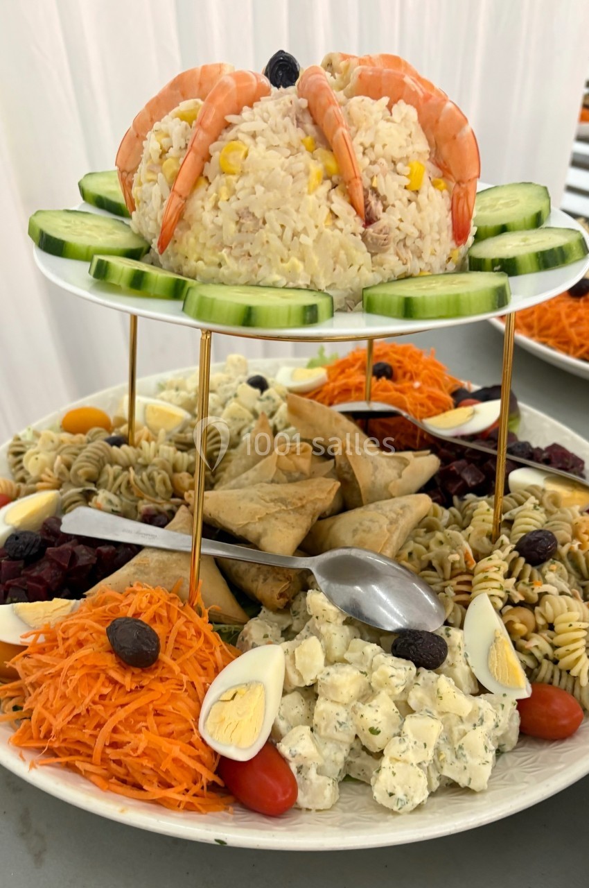 Assiette garnie de riz aux crevettes, crudités, salades variées, samoussas et œufs durs, présentée sur un support à étages.