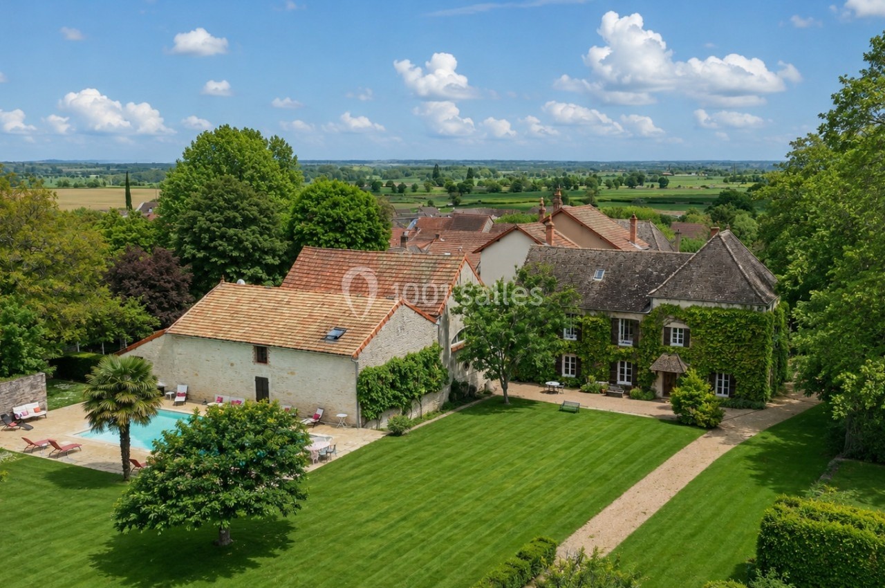 Vue aérienne d'une maison en pierre avec piscine, entourée d'un grand jardin verdoyant et d'arbres, en campagne.