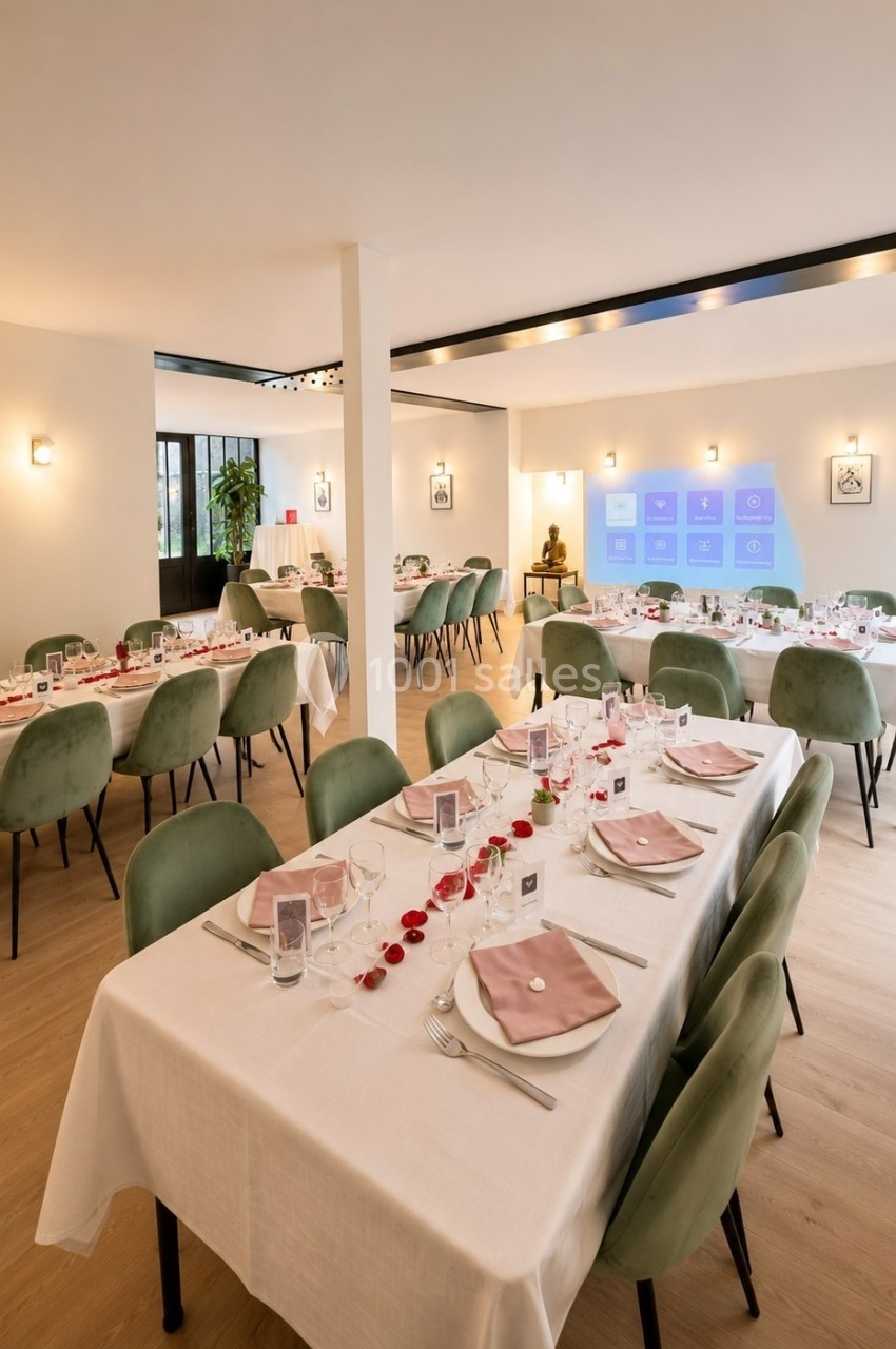 Salle de réception lumineuse avec tables dressées, nappes blanches, chaises vertes et décorations élégantes.
