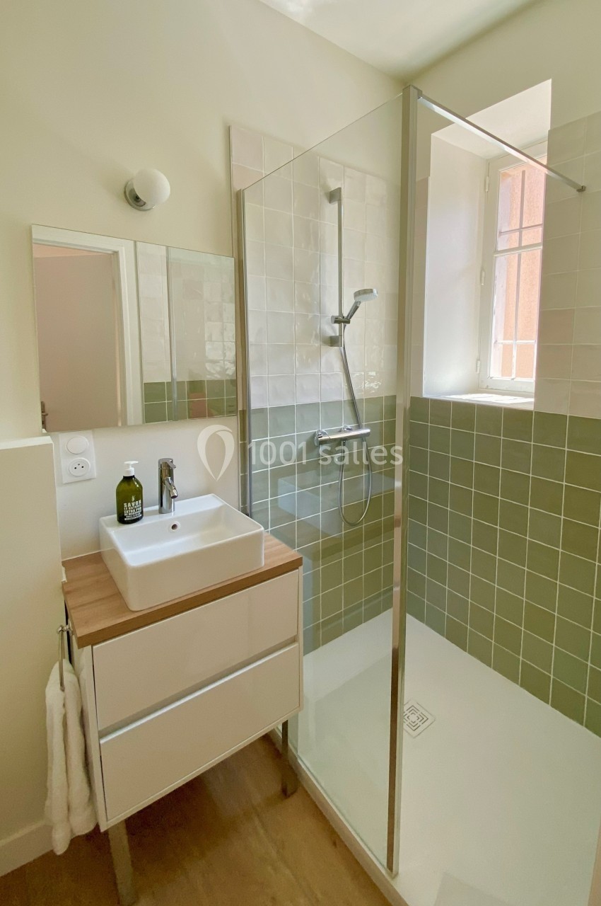 Salle de bain avec douche à l'italienne, meuble lavabo en bois clair et mur carrelé vert et blanc.