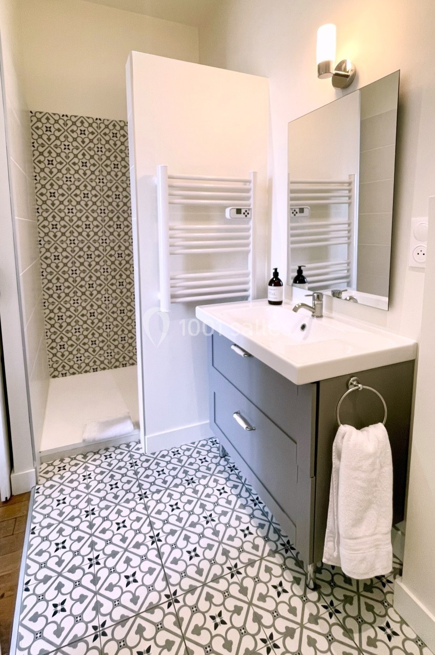 Salle de bain moderne avec douche à l'italienne, meuble vasque gris, miroir et sol en carreaux à motifs géométriques.
