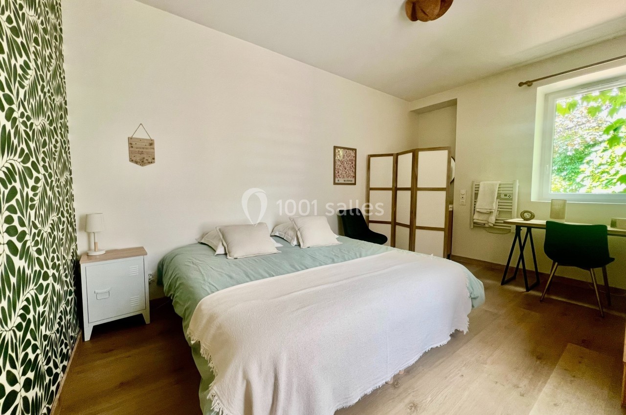 Chambre lumineuse avec lit double, mur décoré de motifs végétaux, bureau près d'une fenêtre et paravent en bois.