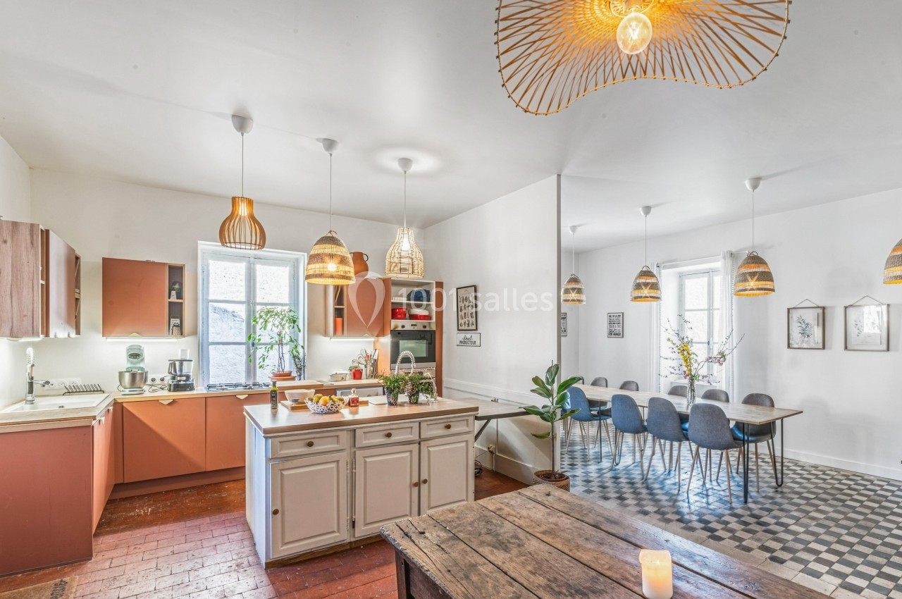 Cuisine ouverte lumineuse avec îlot central, table à manger, suspensions design et grandes fenêtres laissant entrer la…
