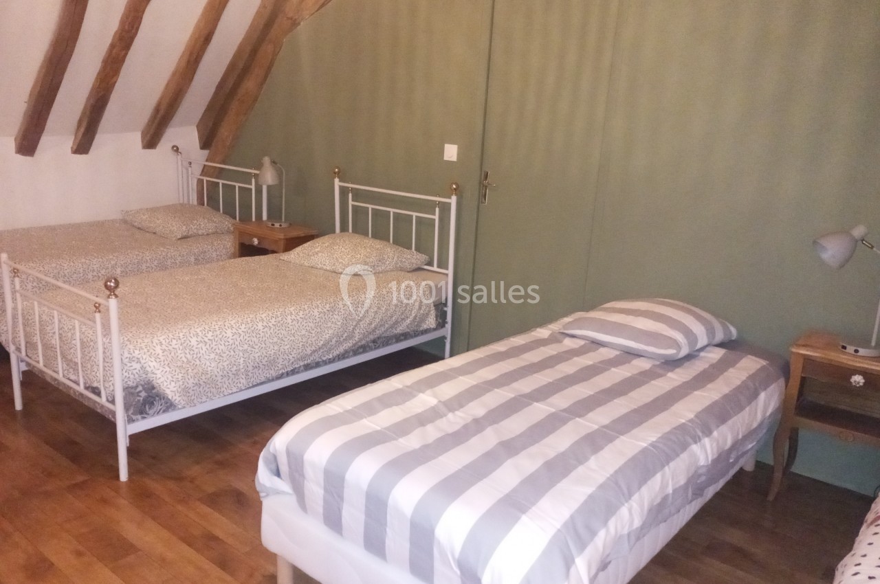 Chambre avec trois lits simples, parquet au sol, murs verts et poutres apparentes au plafond.