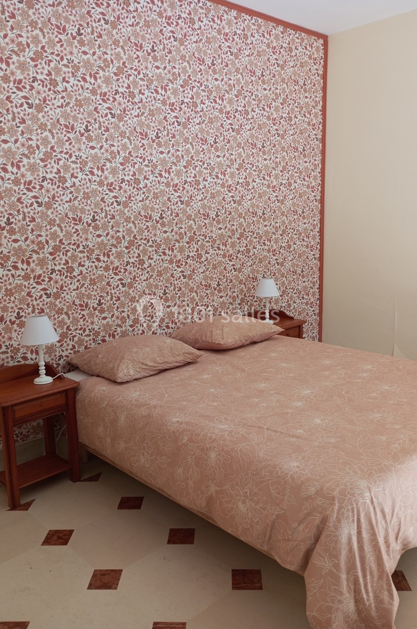 Chambre avec un lit double, couvre-lit beige, tables de chevet en bois et mur décoré d'un papier peint fleuri.
