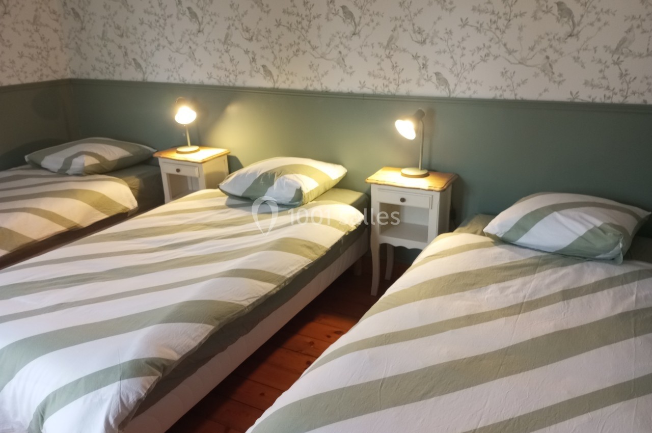 Quatre lits simples avec housses de couette rayées vertes et blanches, éclairés par des lampes de chevet.