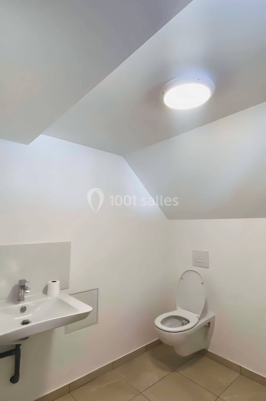 Toilettes modernes avec lavabo, miroir, et éclairage au plafond dans une pièce aux murs blancs et au sol carrelé beige.