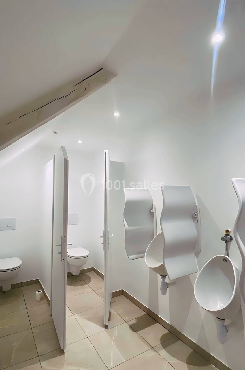 Toilettes modernes avec deux cabines fermées et deux urinoirs muraux sous un plafond incliné.