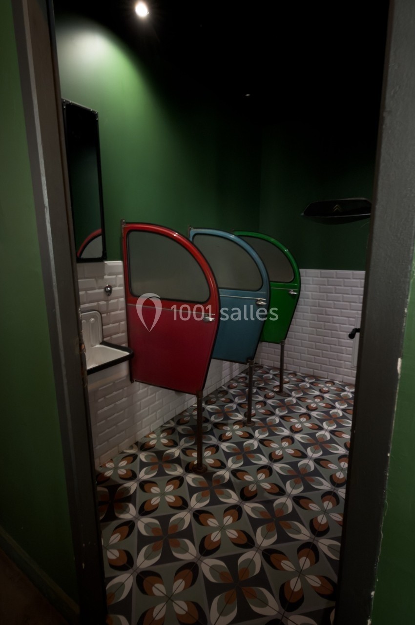 Cabines de toilettes colorées avec portes arrondies, carrelage géométrique au sol et murs verts.
