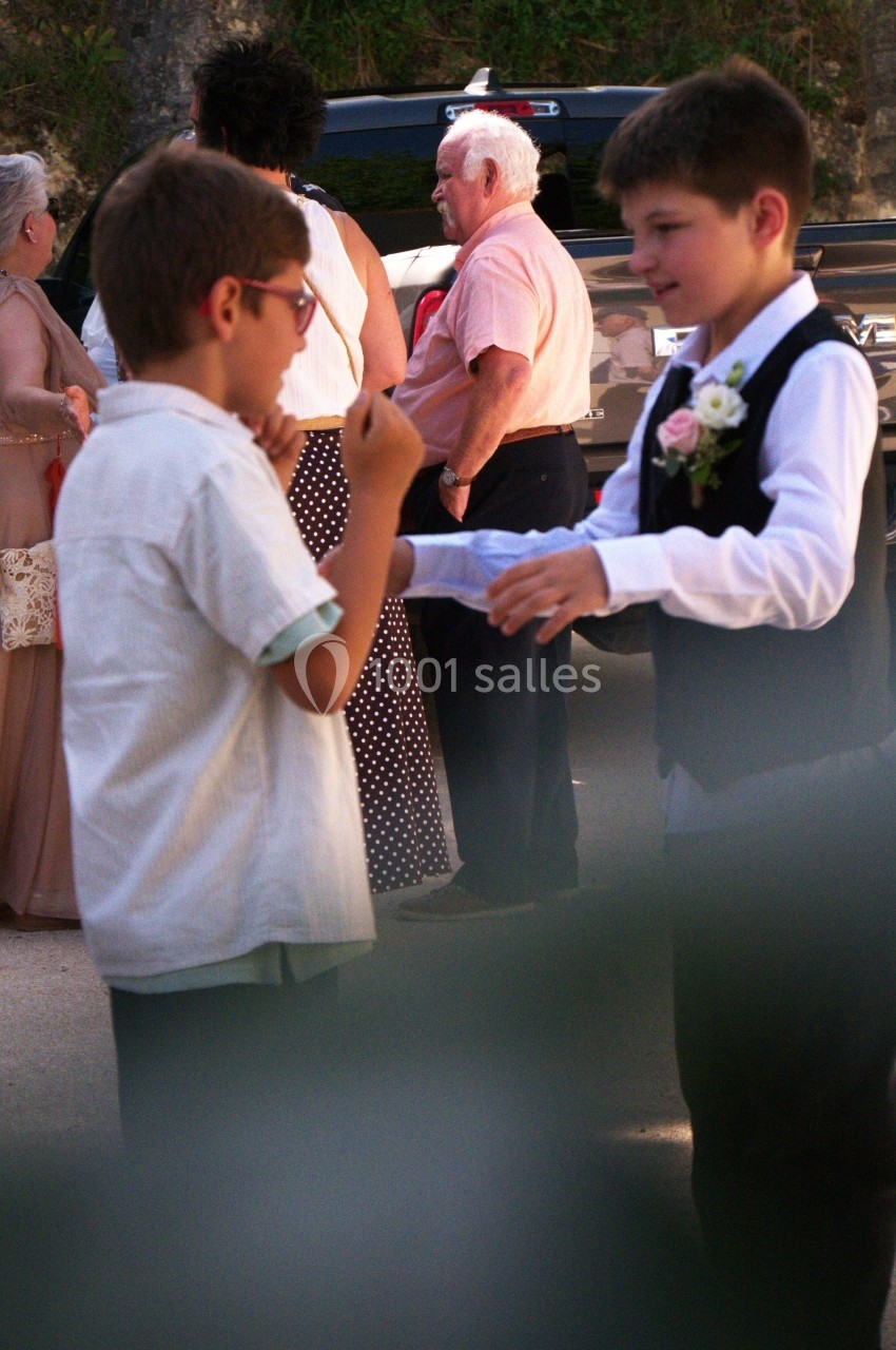 Deux enfants discutent et jouent ensemble en extérieur lors d'un événement, avec des adultes en arrière-plan.