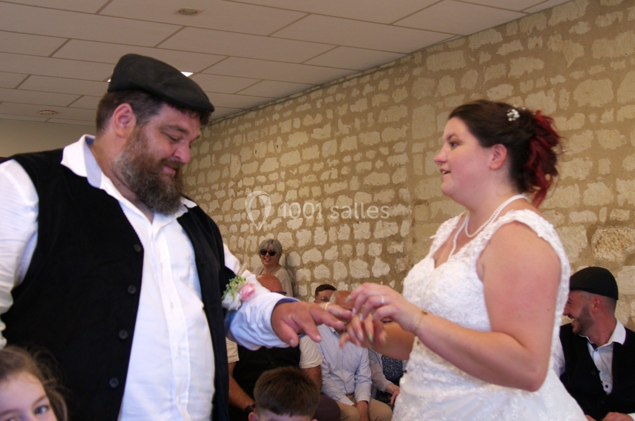 Un couple échange des alliances lors d'une cérémonie de mariage dans une salle aux murs en pierre.