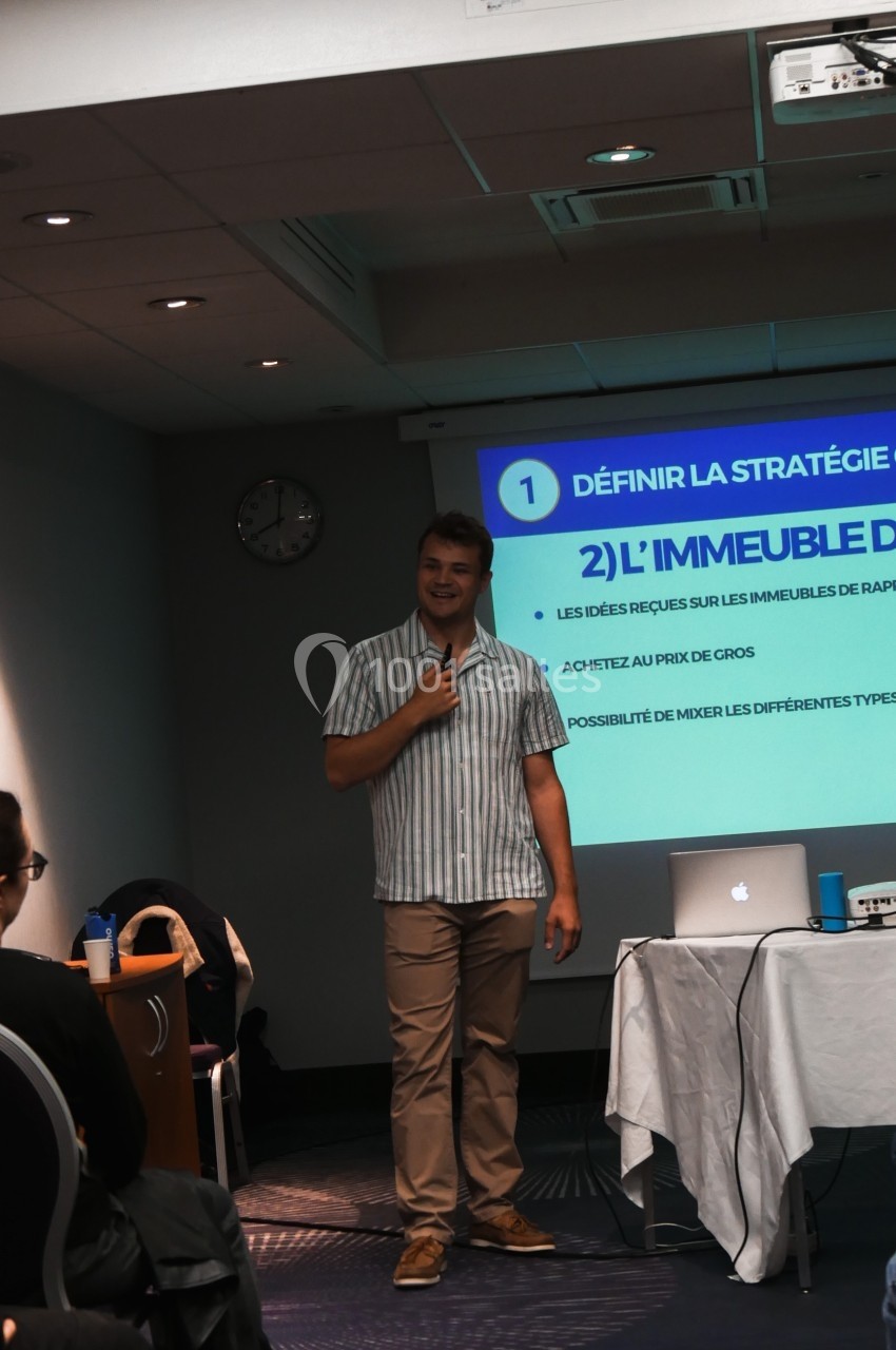 Un homme présente un diaporama dans une salle de conférence, debout devant un écran projetant des diapositives.