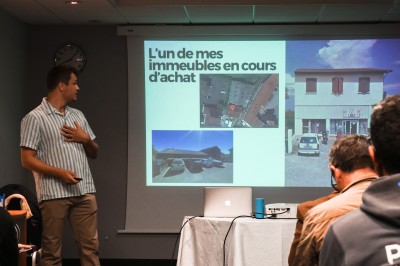 Deux femmes discutent devant un écran dans un espace intérieur avec des éléments en bois au premier plan.