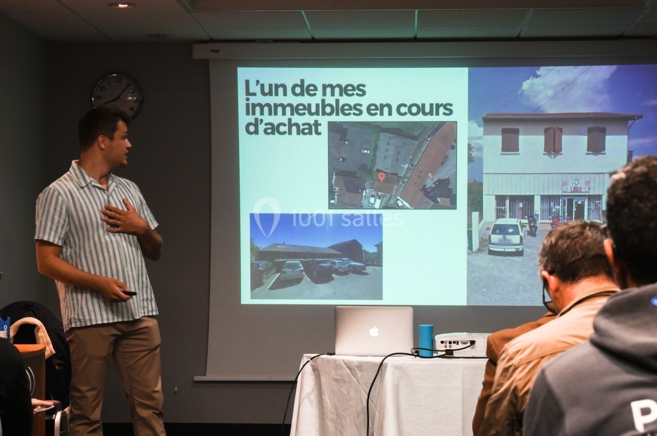Un homme présente un diaporama sur l'achat immobilier devant un petit groupe dans une salle de réunion.