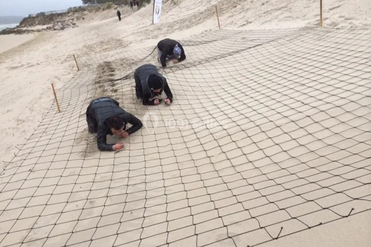 Des personnes rampent sous un filet tendu sur une plage, participant à une activité ou un défi en extérieur.