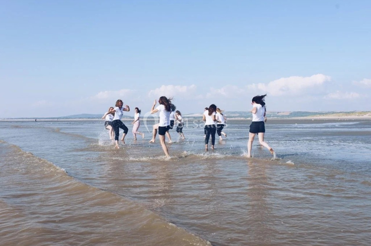 Des personnes courent et jouent dans l'eau peu profonde sur une plage par temps ensoleillé.