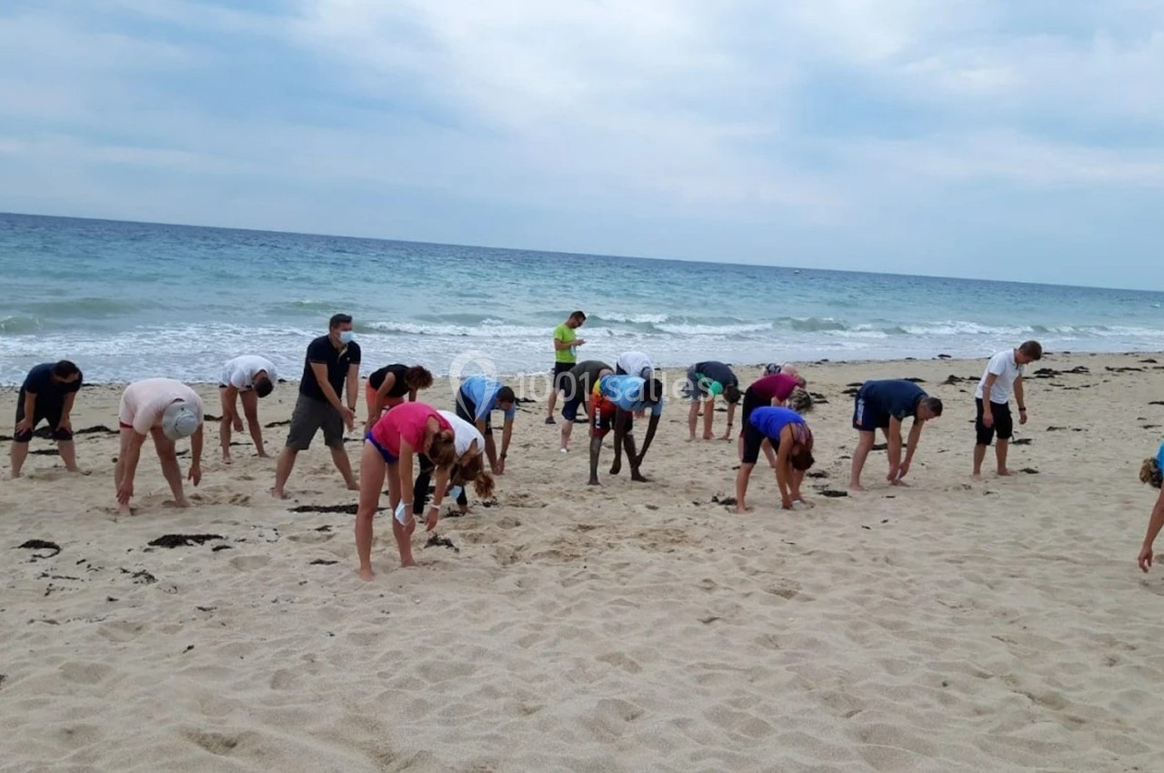 Groupe de personnes s'étirant sur une plage de sable face à la mer sous un ciel nuageux.