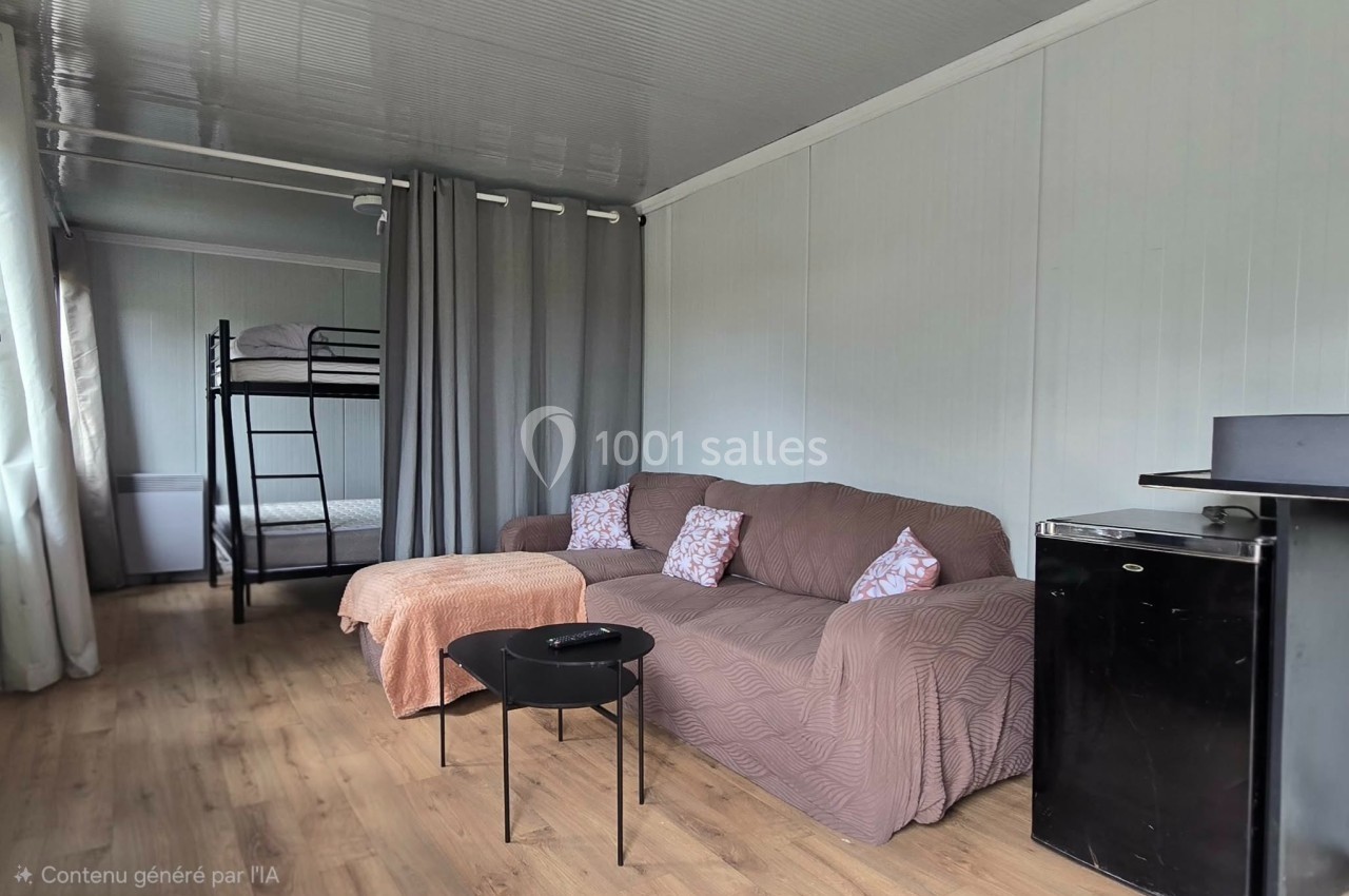 Salon avec canapé, table basse, lit superposé en arrière-plan, rideaux gris et petit réfrigérateur dans un espace lumineux.