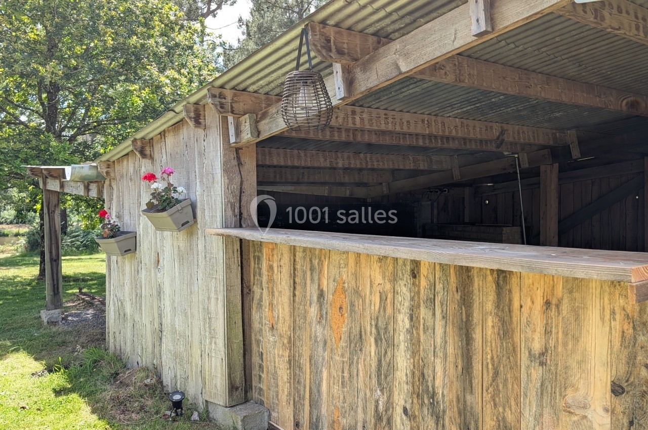 Abri en bois avec un comptoir ouvert, suspendu sous un toit en tôle, entouré de verdure et de jardinières fleuries.