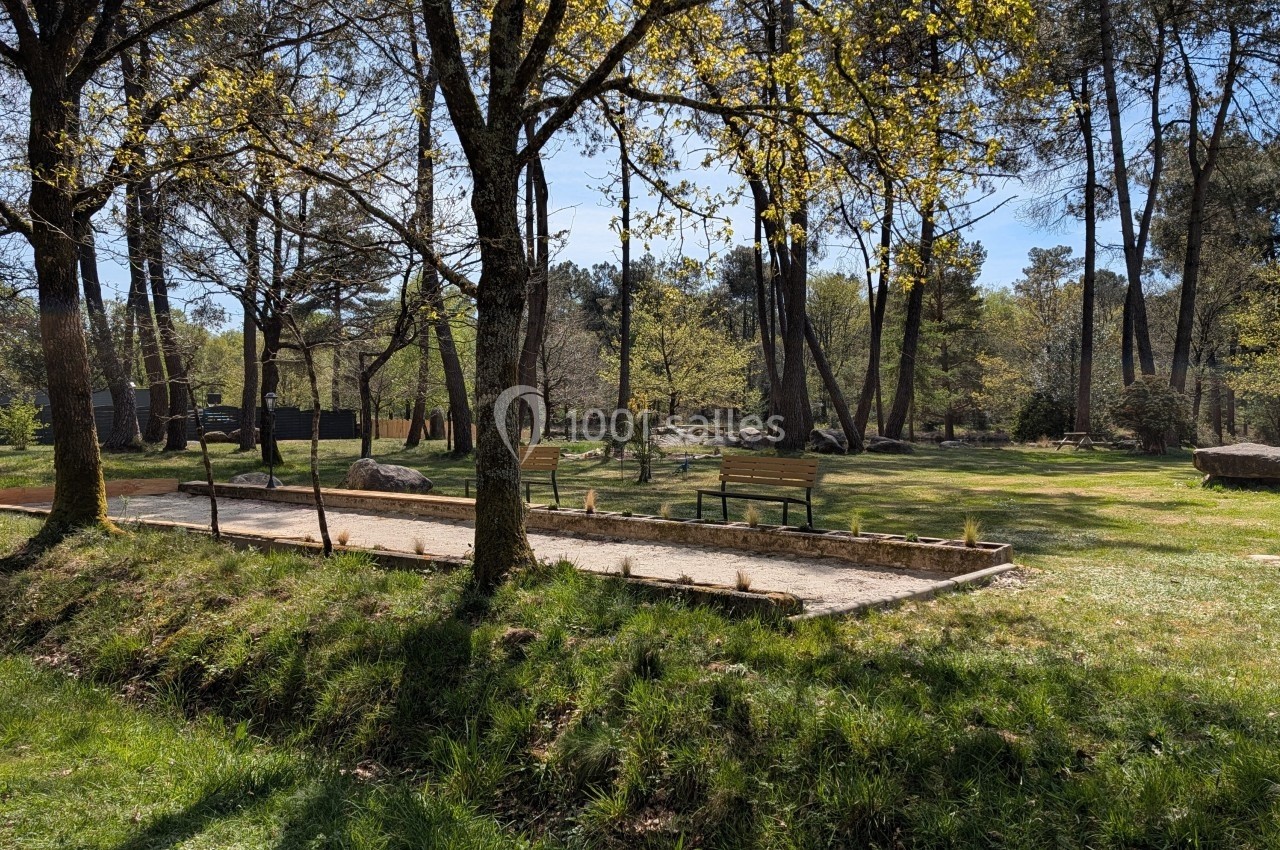 Terrain de pétanque entouré d'herbe et d'arbres dans un parc ensoleillé.