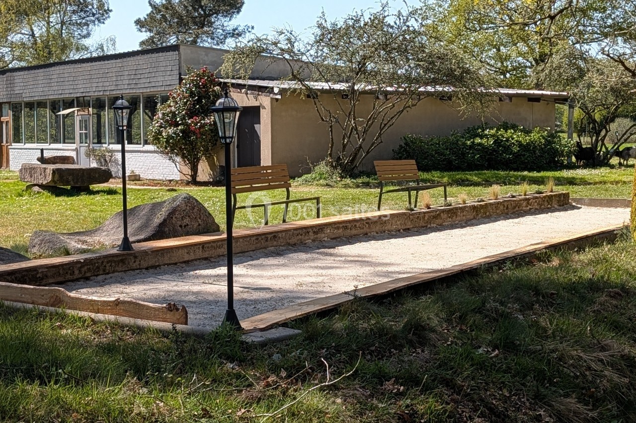 Terrain de pétanque en sable entouré de lampadaires, bancs et végétation, avec un bâtiment en arrière-plan.