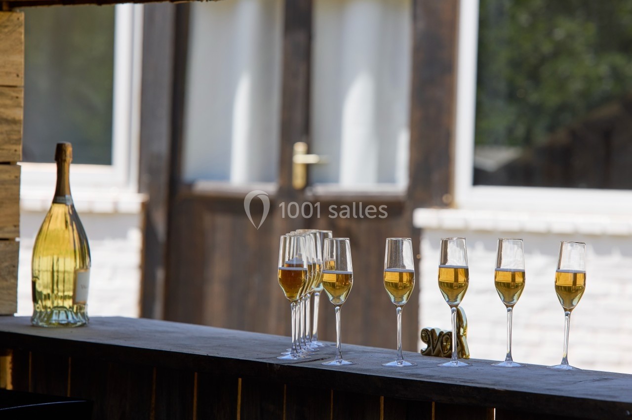 Bouteille et flûtes de champagne alignées sur un comptoir en bois, avec une porte et une fenêtre en arrière-plan.