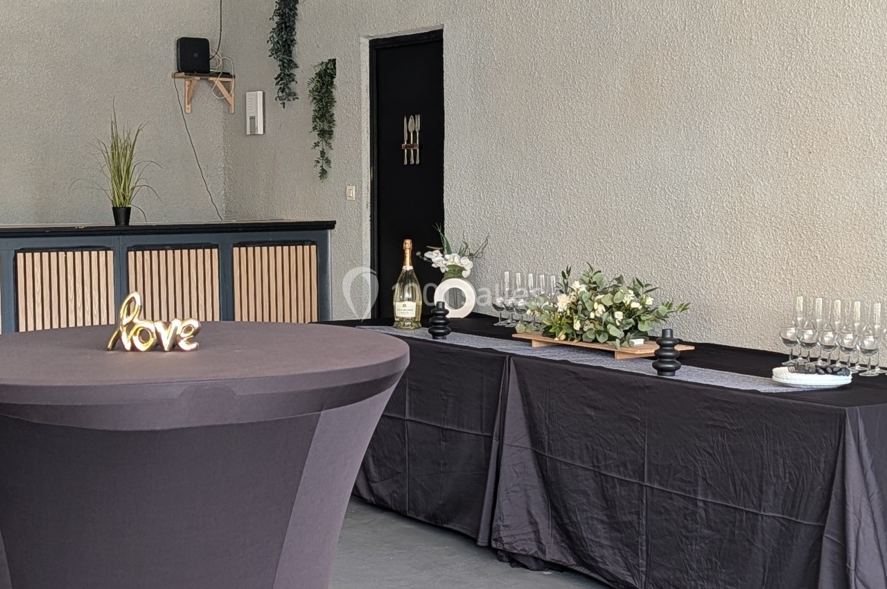 Table décorée avec des fleurs, des verres et une bouteille, devant un bar dans une salle sobrement aménagée.