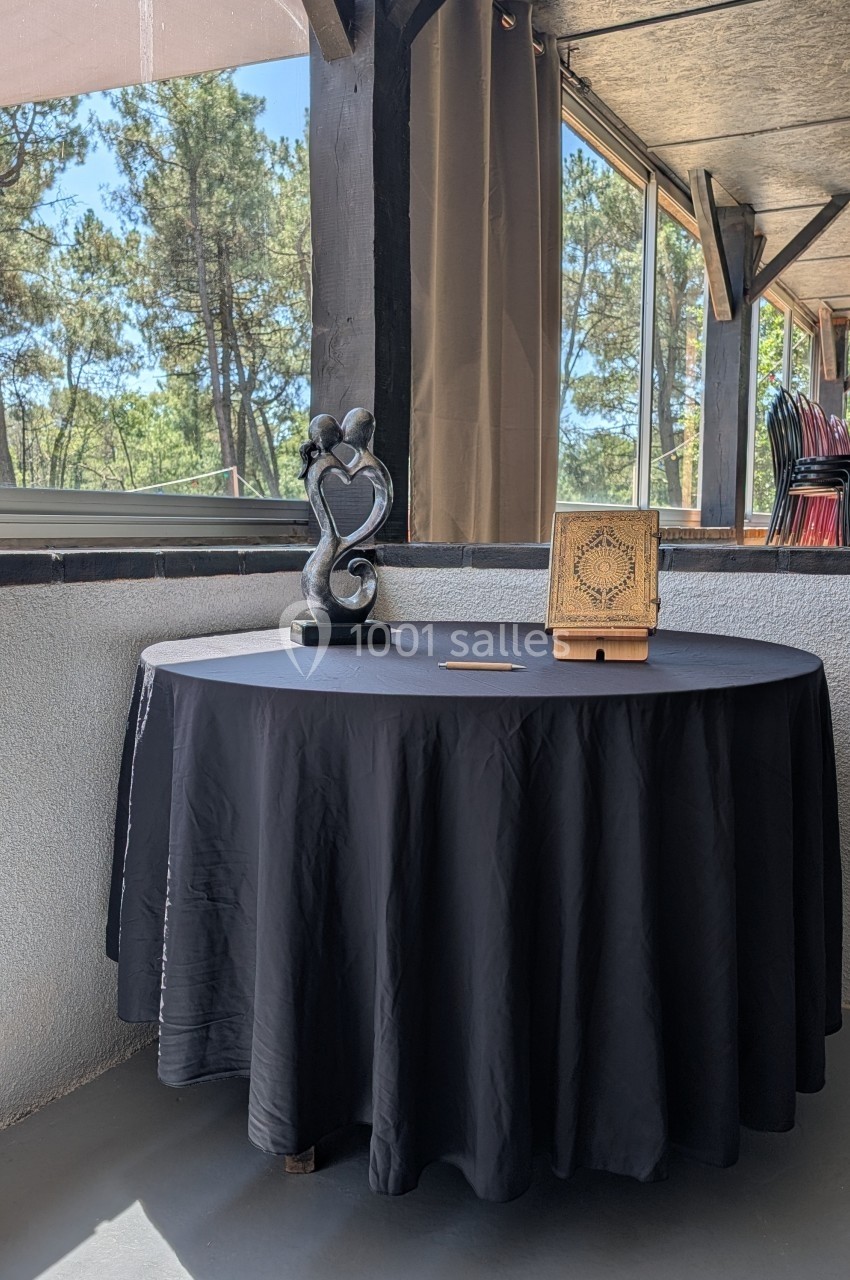 Table ronde noire avec une sculpture en forme de cœur et un livre décoratif en bois, située sur une terrasse lumineuse.
