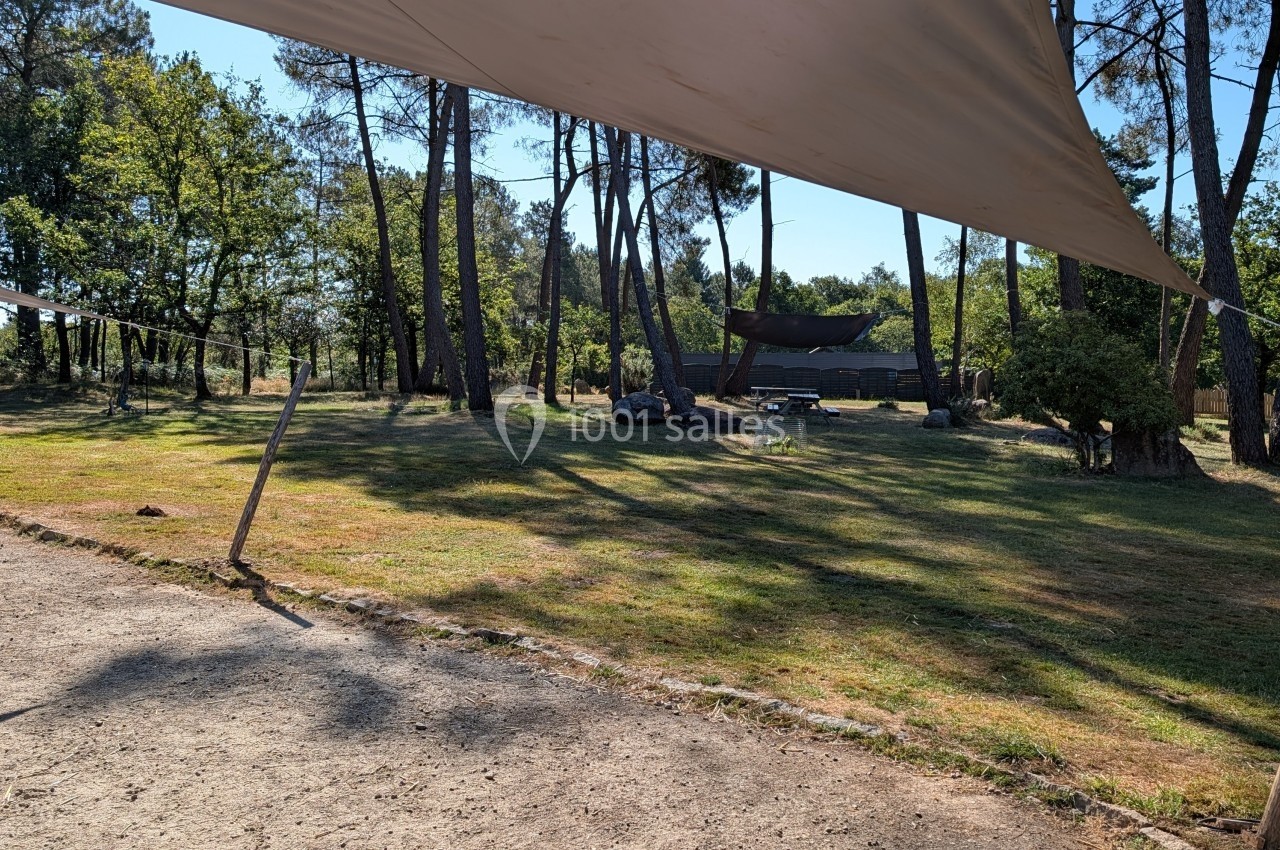 Vue d'un espace extérieur ombragé avec des arbres, des toiles tendues et une cabane en arrière-plan.