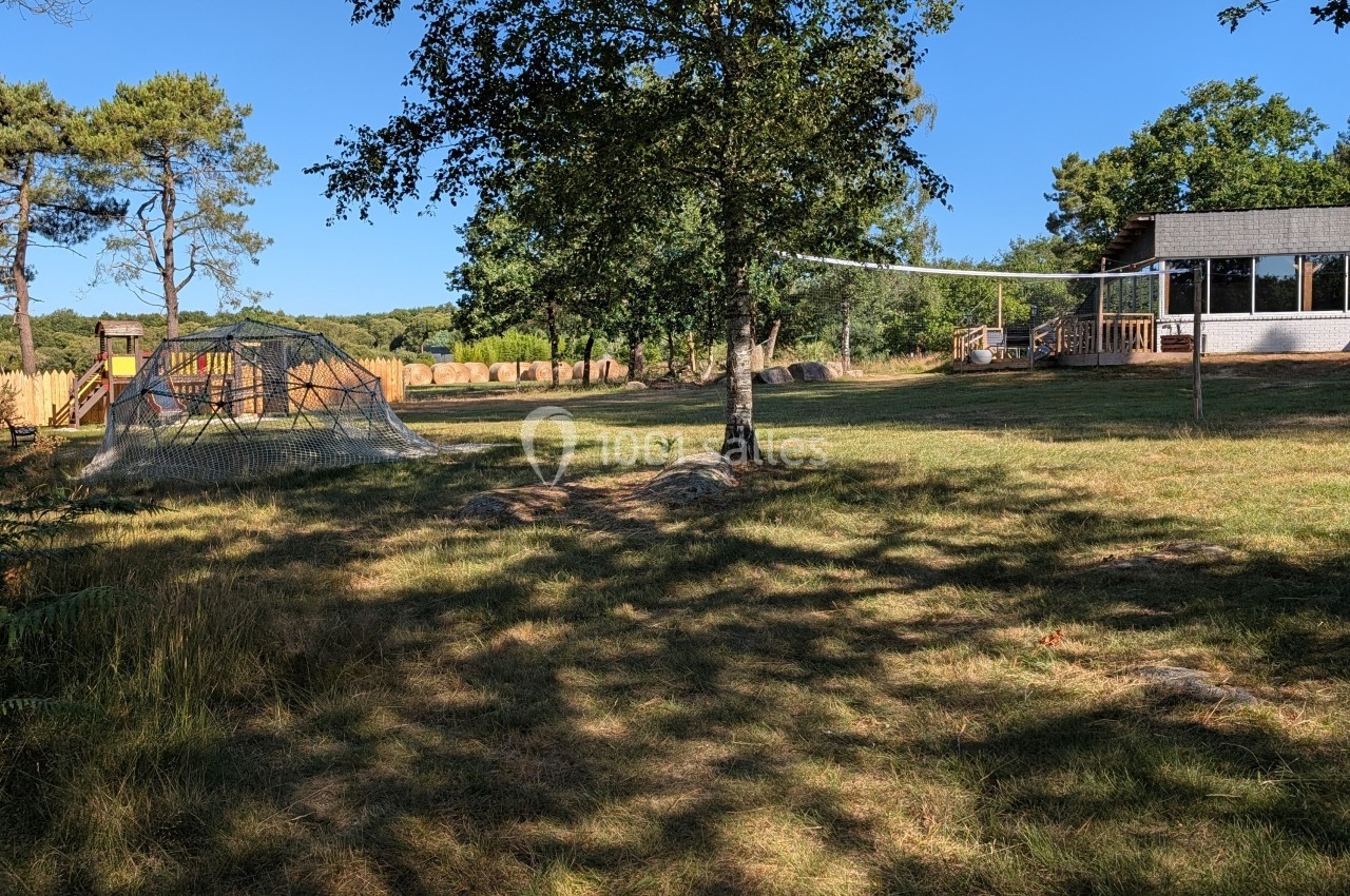 Terrain herbeux avec des arbres, une structure de jeu en filet et un bâtiment en bois sous un ciel dégagé.