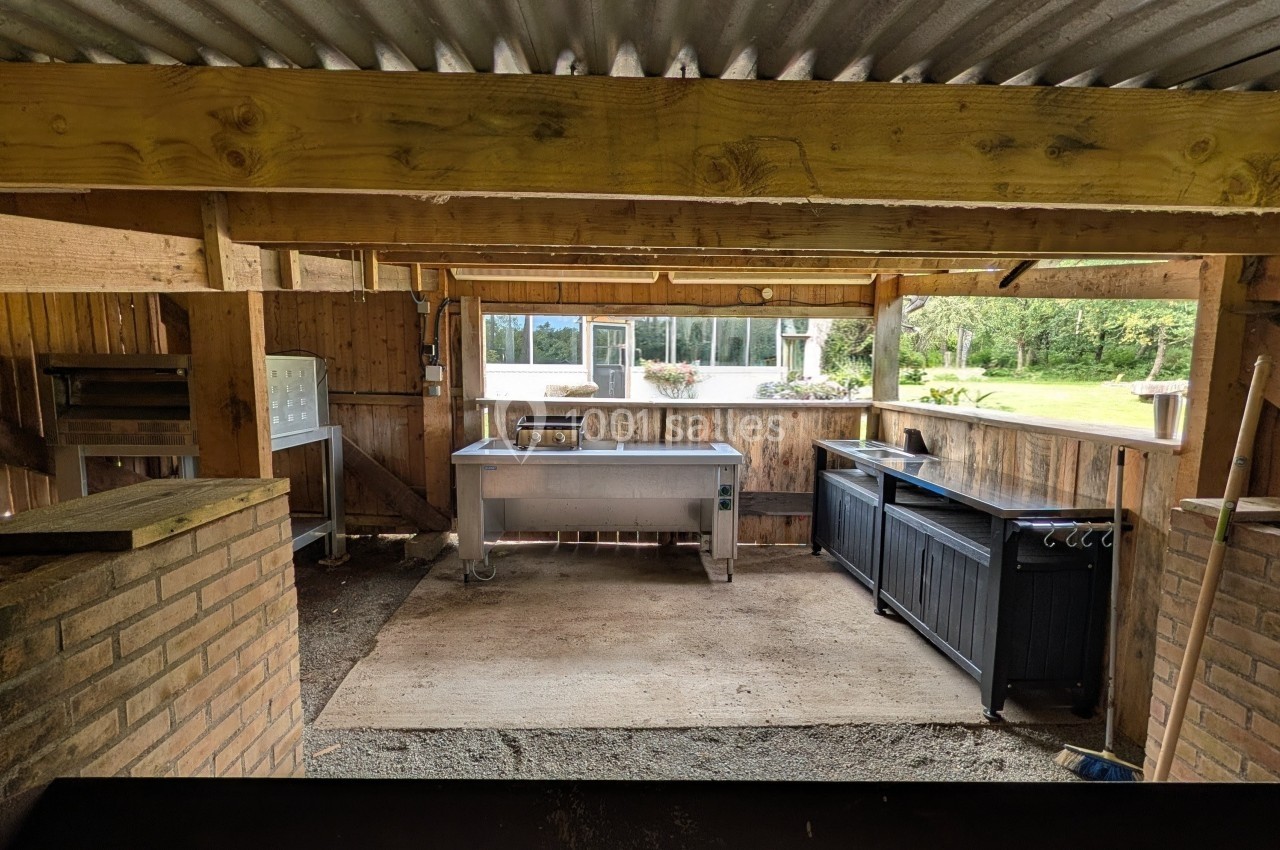 Abri en bois ouvert avec planchas, évier en inox et espace de cuisson, donnant sur un jardin verdoyant.
